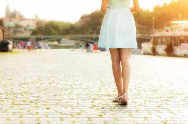 woman in spring dress walking away from camera on a cobblestone street along a river